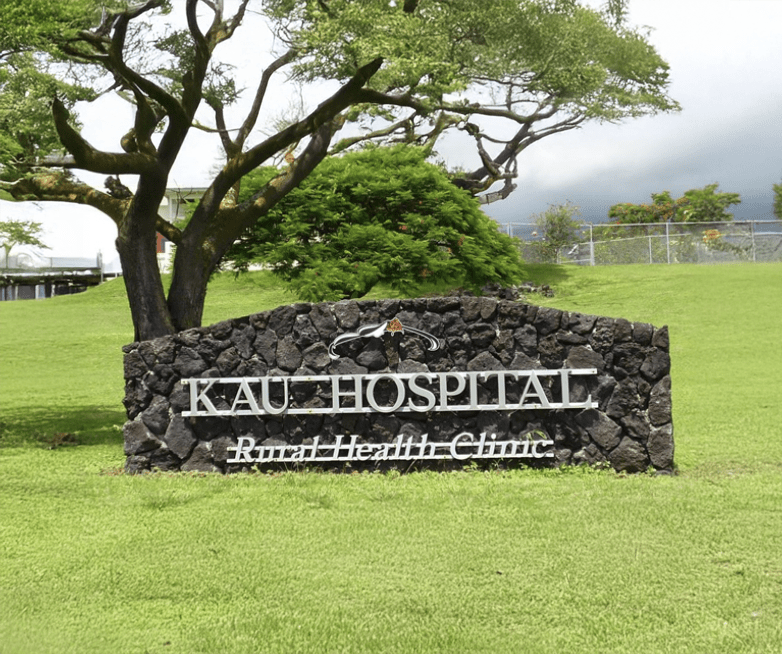 Kau Hospital sign in a grassy area, showcasing its commitment to rural health care services amidst a lush landscape.