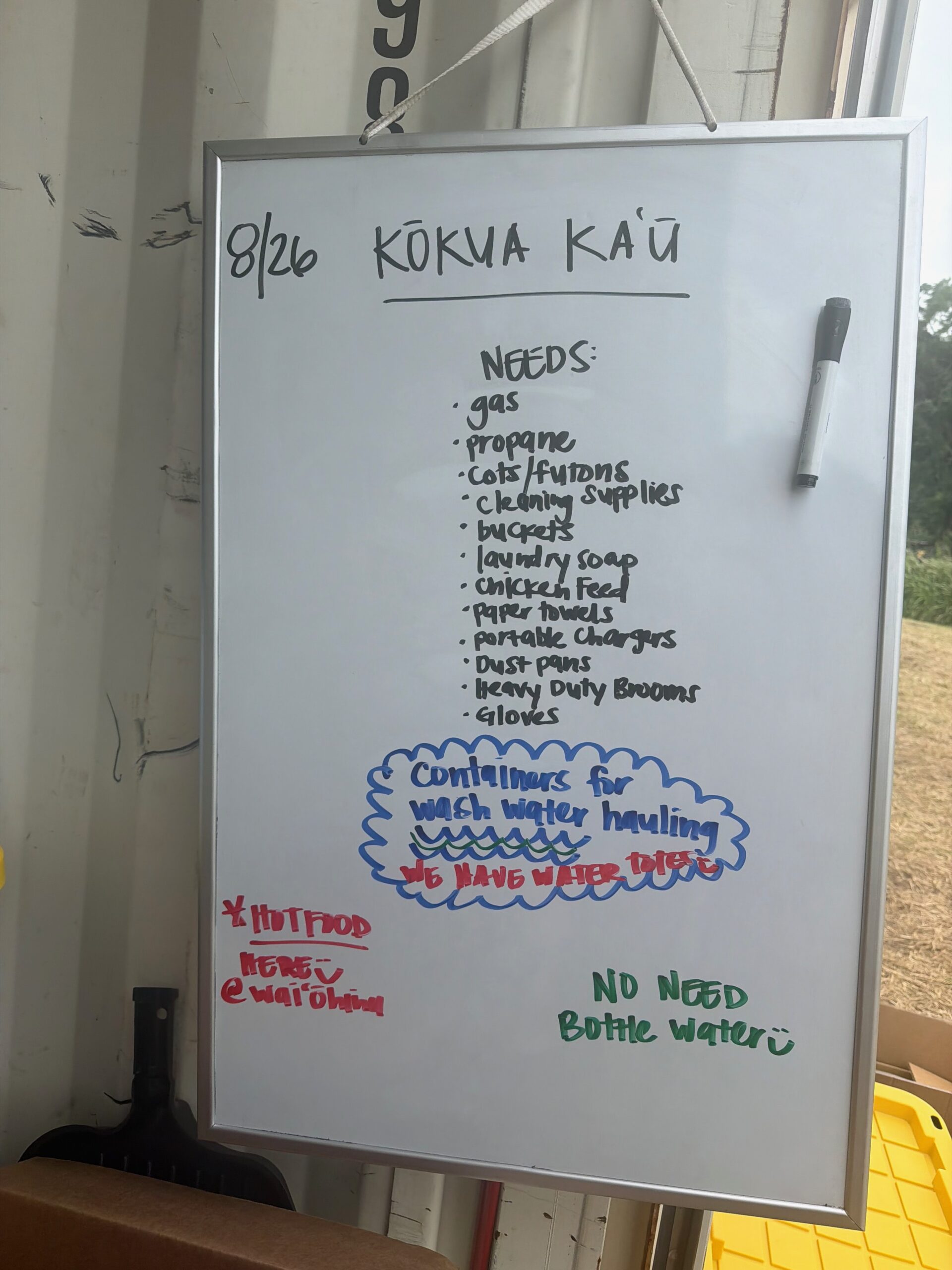 Handwritten whiteboard dated 8/21 headed Kokua Kau, listing community needs including canned food, hygiene products, propane, portable stoves, gas, baby items, paper goods, pet food and cleaning supplies.