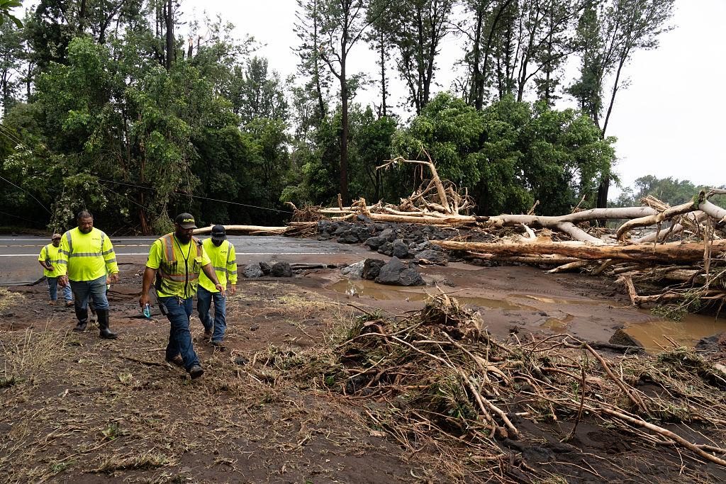 County crews walk past uprooted trees and mud washed across Highway 11 in Kaʻū after Hurricane Lala.