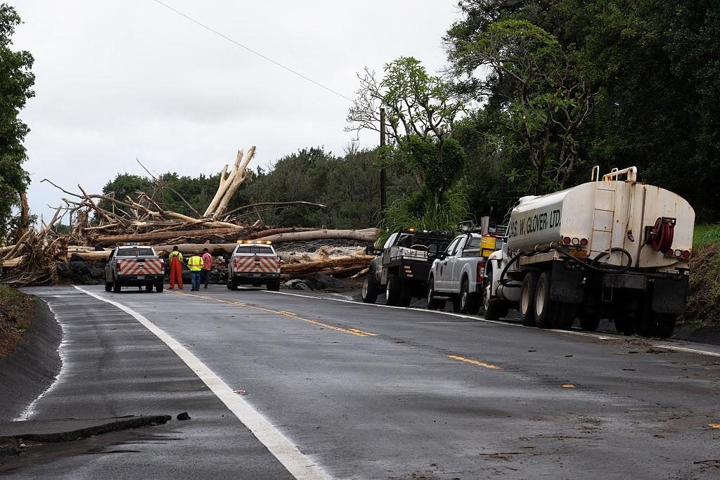 Downed trees block a lane of Highway 11 in Kaʻū as road crews and a water tanker stage nearby.